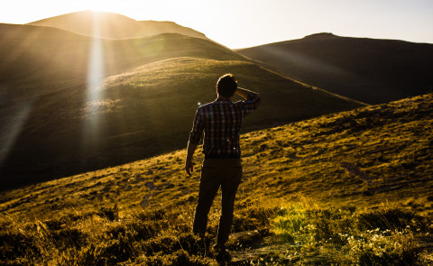 wanderer searching for something and looking into the sun over green hills